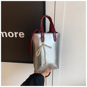Détail du sac à main argenté avec nœud en perles, poignée rouge et texture PU brillante