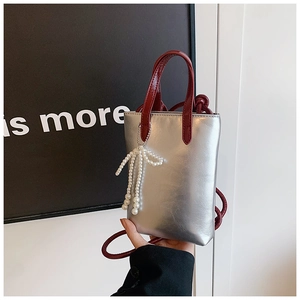 Vue détaillée du mini sac argenté avec poignées rouges et pendentif nœud perlé