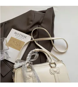 Detail of cream Boston bag featuring ribbon bow handle and adjustable long strap