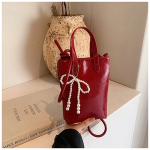Détail du mini sac seau rouge brillant avec breloque nœud en perles blanches et poignées