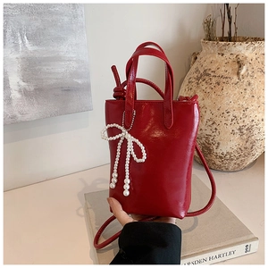 Détail du sac à main rouge verni avec nœud en perles posé sur des livres anciens