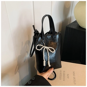 Détail d'un sac seau noir brillant orné d'un pendentif en perles blanches en forme de nœud