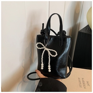 Détail du sac seau en cuir noir brillant avec un élégant nœud en perles blanches