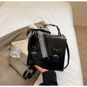 Close-up of black patent leather Lolita style handbag with lace bows and ribbon detail