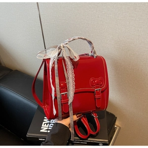 Detail of red shiny patent leather backpack with white lace bow and plaid handle wrap