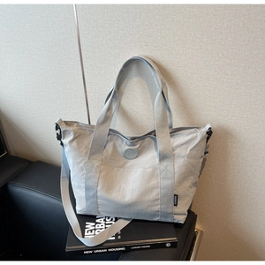 Détail du sac fourre-tout gris clair avec écusson logo rond et bandoulière réglable