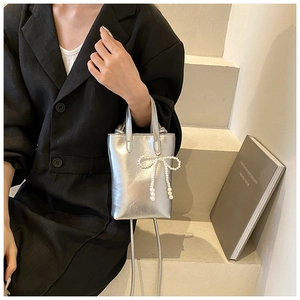 Détail d'un mini sac seau argenté métallisé avec nœud en perles et bandoulière chaîne