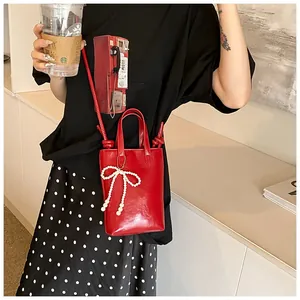 Détail du mini sac seau rouge en cuir brillant avec élégante breloque nœud en perles