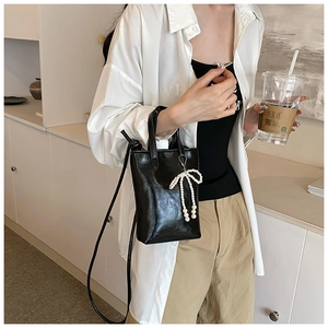 Détail du sac seau noir brillant avec un pendentif nœud en perles blanches sur l'anse