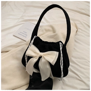 Close-up of black corduroy handbag featuring a large cream silk bow and drawstring details
