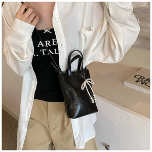 Détail d'un sac à main en cuir verni noir avec nœud en perles blanches et bandoulière