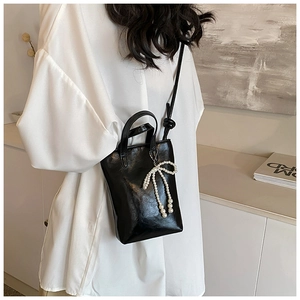 Détail d'un sac seau noir brillant avec nœud en perles et élégante bandoulière chaîne