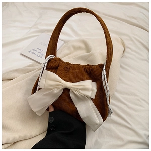Close-up of brown corduroy handbag with a large white bow and woven rope handle