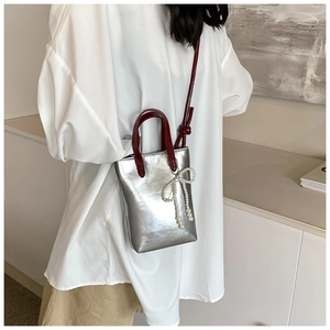 Détail du sac à main argenté avec poignées bordeaux et breloque noeud en perles