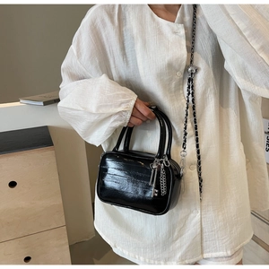 Dettaglio mini borsa in vernice nera con ciondolo chiave argento e tracolla a catena