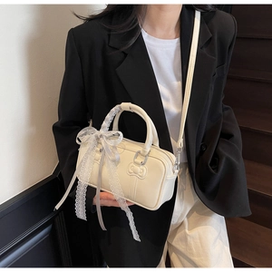 Side view of cream Boston bag with lace bow accessory held by model in black blazer
