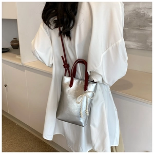 Détail d'un mini sac argenté avec anses rouges et nœud en perles porté par un mannequin