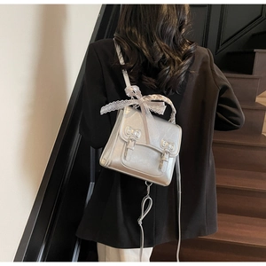 Detail of silver metallic crossbody bag with white lace bow and dual buckle closure
