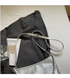 Detail of silver woven underarm bag with adjustable strap and metal chain on a blazer