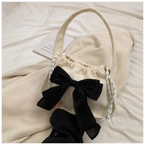 Detail of cream corduroy bucket bag featuring a large black bow and striped drawstring