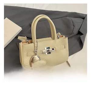 Detail showing silver metal twist lock and heart charm on beige pebbled leather handbag