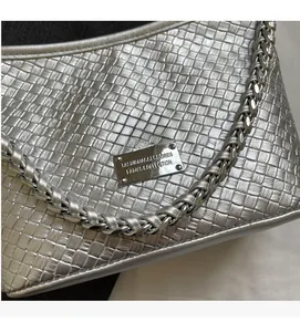 Macro shot of silver woven leather texture and metallic logo plate on shoulder bag