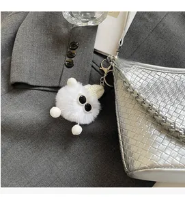 White fuzzy monster bag charm with knit hat on silver woven tote bag detail
