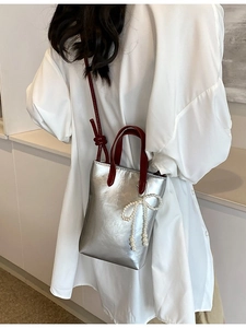 Sac seau argenté avec anses rouges et nœud en perles présenté par un mannequin