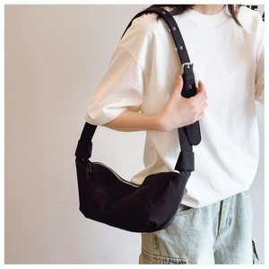 Detail of black pleated half-moon shoulder bag showing the nylon texture and wide strap