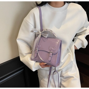 Close-up of shiny purple crossbody bag with bow accents and lace ribbon handle