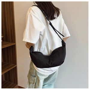 Close-up of black crescent nylon shoulder bag with adjustable eyelet strap on a model