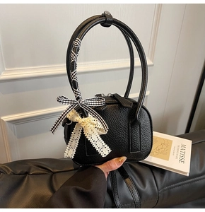 Dettaglio borsa nera in pelle a grana con manico lungo e decorazioni a fiocco eleganti