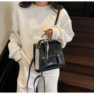 Detail of black glossy leather crossbody bag featuring white lace bow and ribbons