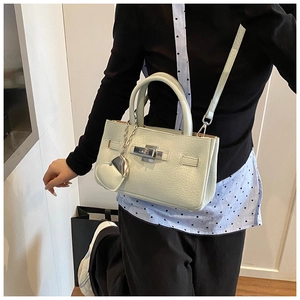 Detail of light green pebbled leather handbag with metallic turn-lock and heart charm
