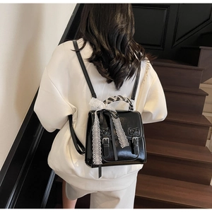 Detail of a black PU mini backpack with lace bows and silk scarf handle on wooden stairs