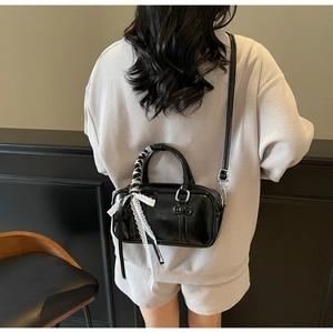 Detail of black patent leather handbag featuring lace bow ribbon and slim shoulder strap