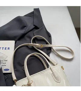 Détail d'un sac seau en cuir verni blanc avec bandoulière réglable sur un blazer gris