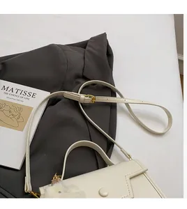 Piccola borsa quadrata bianca su blazer grigio con fibbia dorata e ciondolo a coniglio