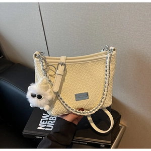 Close-up of cream woven bucket bag with silver chain strap and plush monster charm