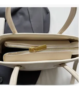 Gros plan sur la fermeture éclair dorée et le cuir ivoire texturé du sac à main