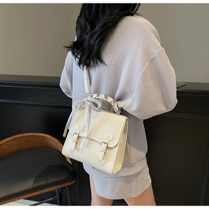 Detail of creamy white satchel featuring decorative bows and lace-wrapped handle detail