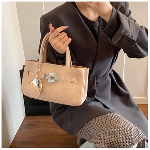Detail of apricot leather handbag with silver lock and heart charm held by a model