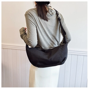 Detail of black pleated half-moon shoulder bag with wide strap on a female model
