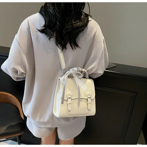 Detail of cream PU leather backpack featuring decorative bows and lace ribbon handle
