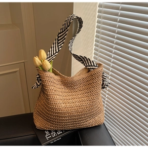 Détail du sac cabas en paille avec bandoulières rayées et texture de nœud rustique
