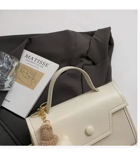 Dettaglio borsa crema con patta geometrica e ciondolo a forma di orsetto in maglia marrone