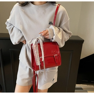 Close-up of red patent leather crossbody bag with white lace bow on grey tracksuit