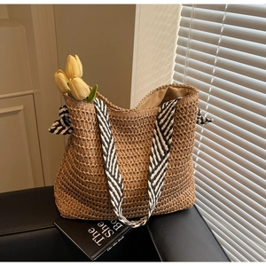 Détail du sac cabas en paille tissée avec bandoulière rayée noir et blanc sur canapé