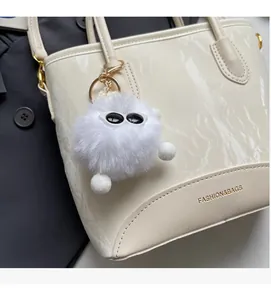 Détail d'un sac à main crème effet marbre avec breloque peluche sur veste grise