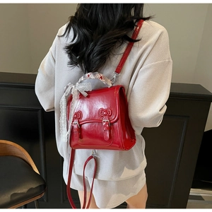 Detail of red patent leather backpack with silk scarf handle and lace bow charm
